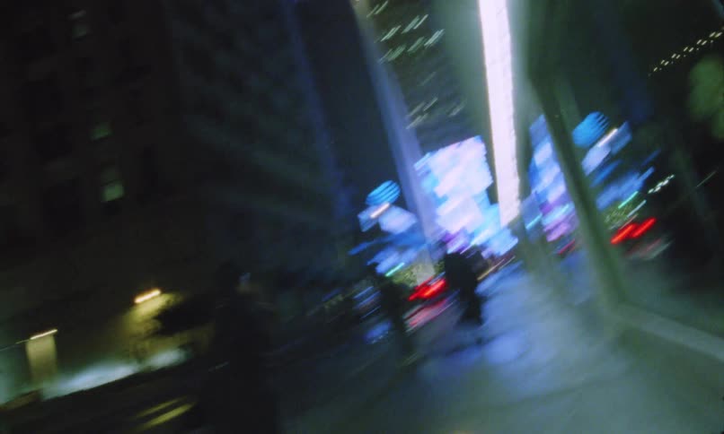 Two people wearing dark clothing are jogging on a sidewalk one night in the city
