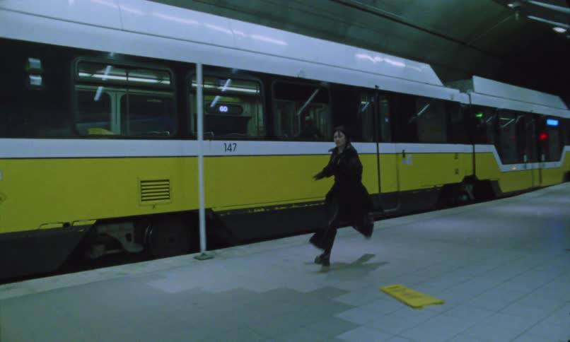A person runs along a subway platform beside a yellowandwhite train pulling through the station