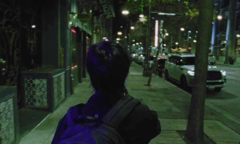 Young male person dressed in black and carrying a backpack walking on the streets of a metropolitan area during night time