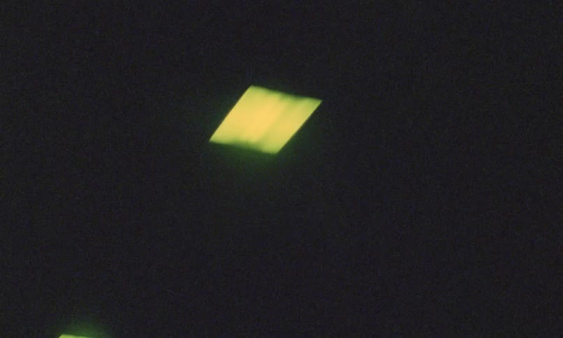 Small yellow squares of light glow softly against a dark grainy background with a brief flash of a truck