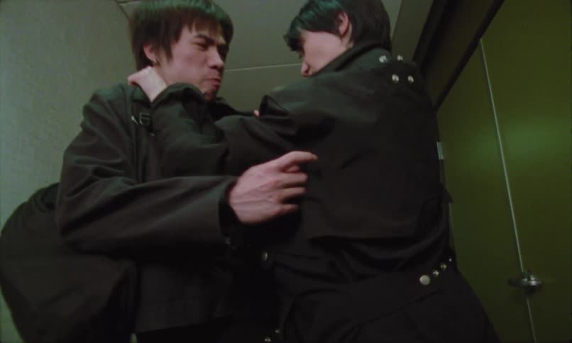 Two men both dressed in dark clothing are physically engaged in what appears to be a confrontation or struggle in a narrow hallway one man has his hand around the others neck area as they face each other aggressively