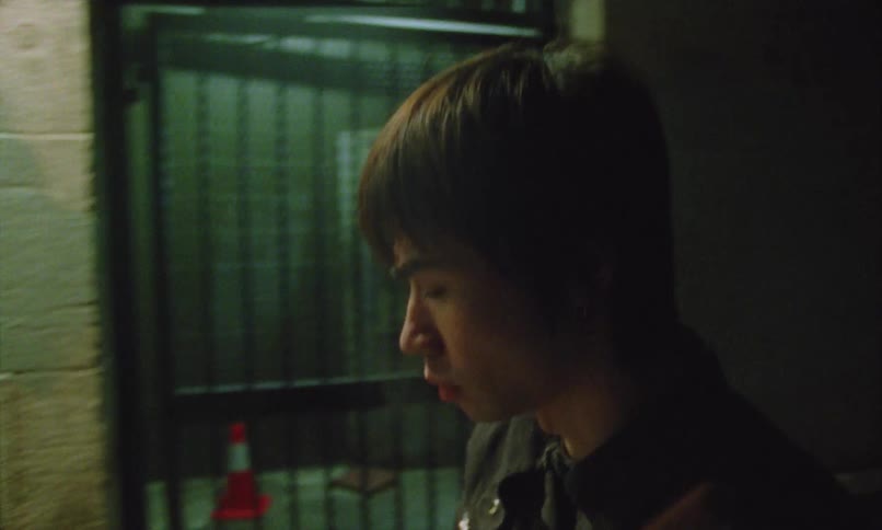 Man smokes in a corridor lit by cool lights near a metal fence