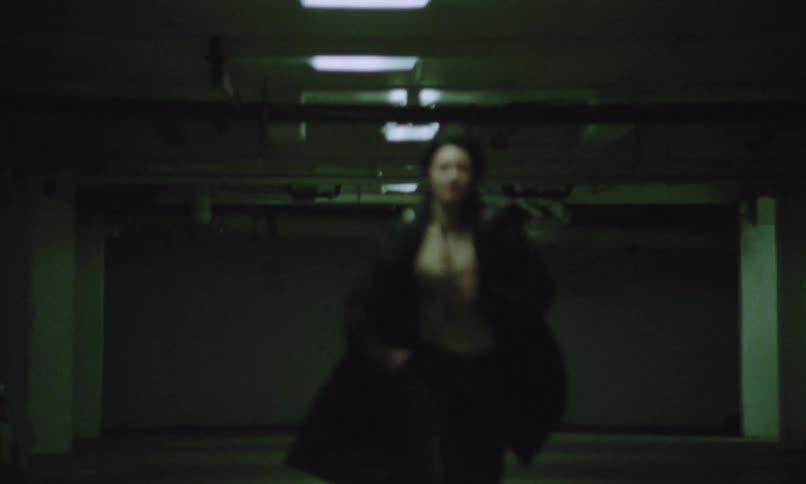 Woman runs through an underground parking lot with a determined expression