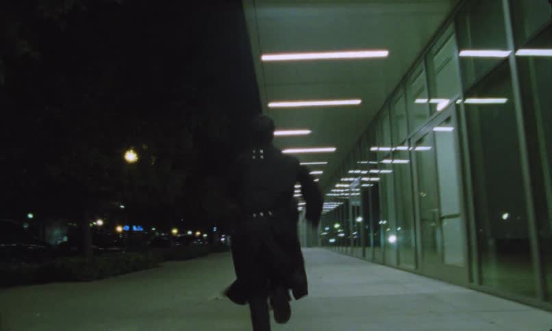 Two people running on a sidewalk next to a building with glass windows at night