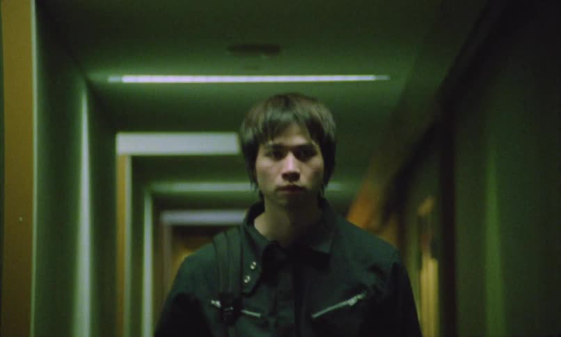 A man in a black jacket walks through a dimly lit corridor