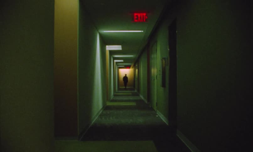 The silhouette of a person walking down a corridor with green lights and a red sign