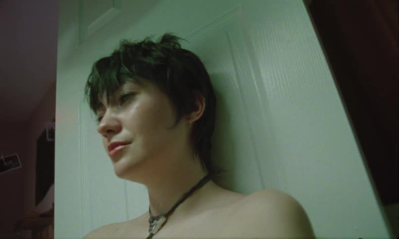 A young woman with short dark hair leans against a door flashes from a camera are visible