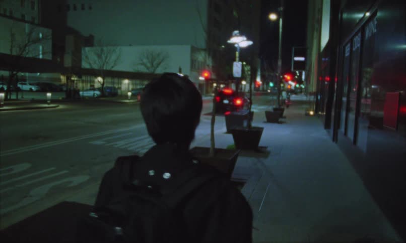Person walks alone down a lit street at night with a backpack on