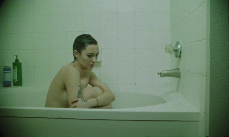 A woman sitting in a bathtub curled up and looking sad