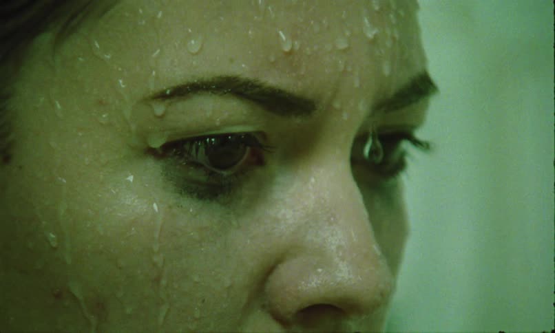 A woman with wet skin and smudged eye makeup looks downward with a tired sad expression
