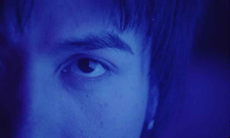 Blue lighting tints the skin and face of a man as he stares