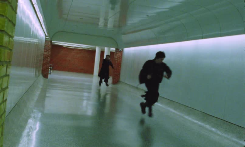 Two men run along a wide corridor in a commercial building