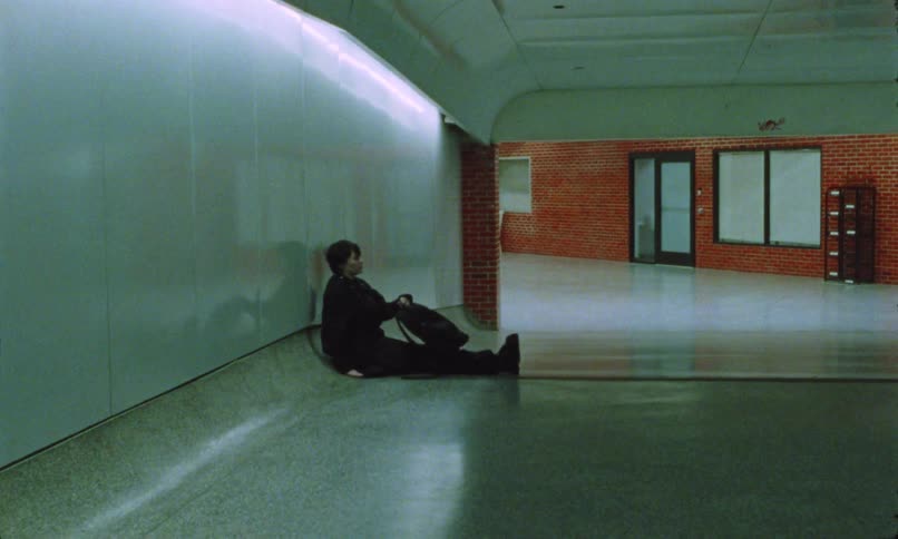 Person sits against the wall in an empty quiet hallway