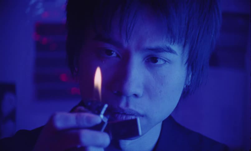 The face of a man staring intently at the flame of a lighter and the surrounding environment is entirely blue