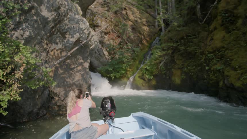 Woman in boat taking photographs with cell phone of waterfall