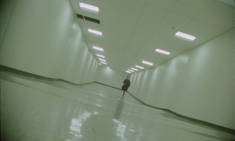 Person runs through a white hallway lit by fluorescent lights
