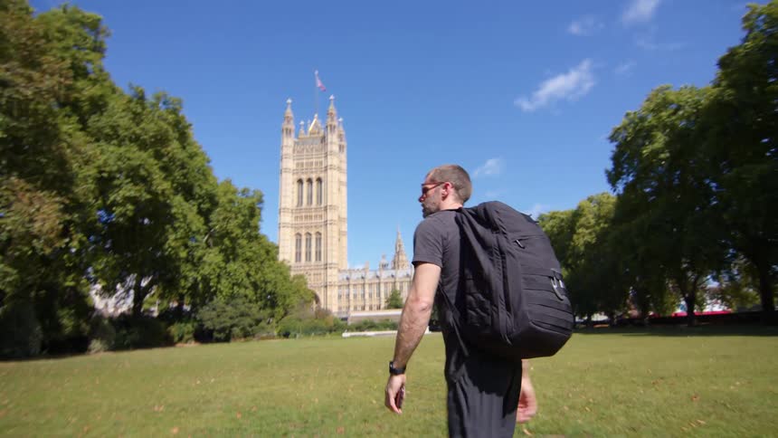 A man in a black shirt is walking in a park with a large building in the background