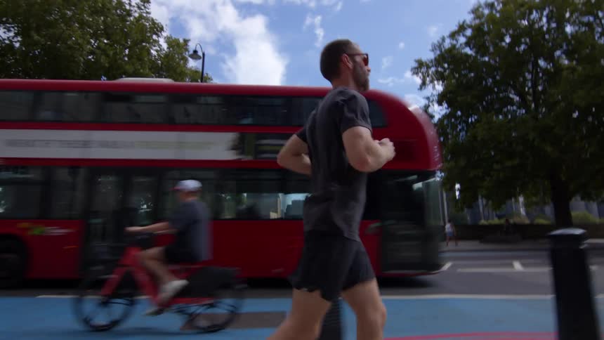 Man jogging on a city street as a red bus passes by