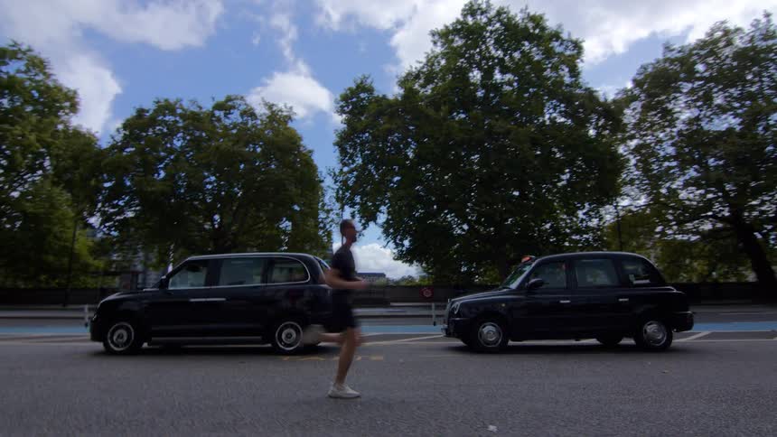 Man runs on a street lined with black taxis under a partly cloudy sky