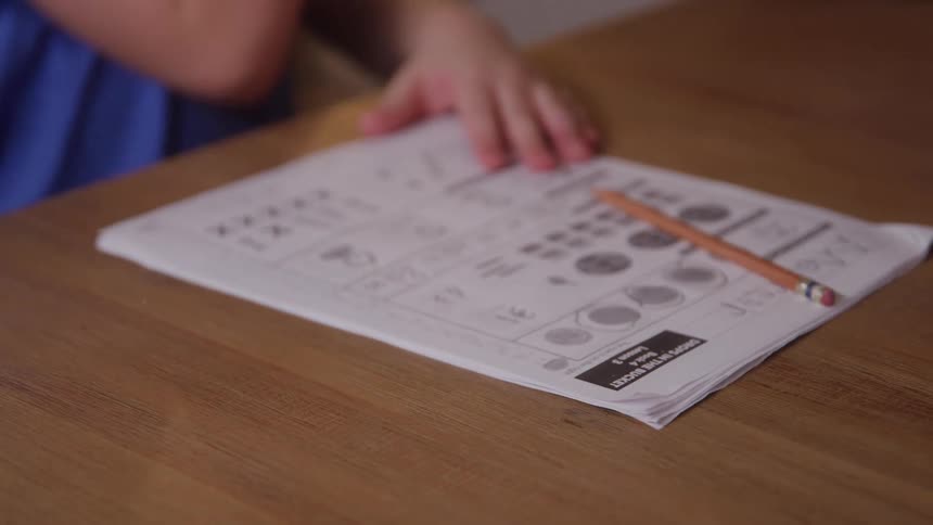 A child sits at a table with a mathematics worksheet in front of them