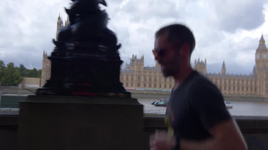 A man wearing sunglasses is running while smiling and behind him is a large tourist building