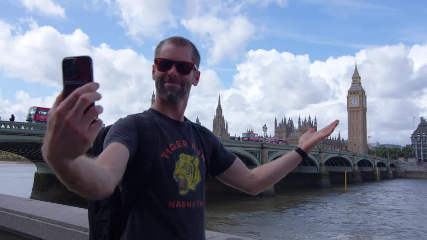 A male tourist taking phone selfies while standing outdoors in a city during daytime