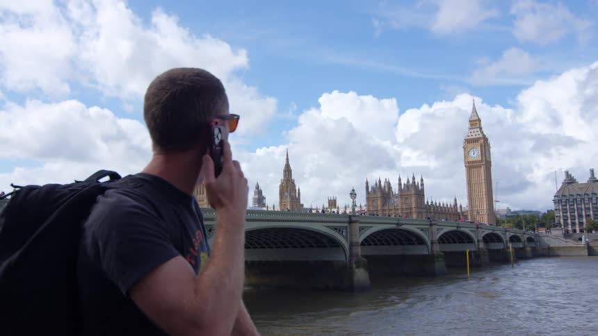 Man talks on the phone near the river with big ben in the background