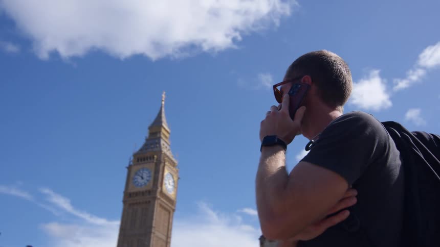 Man talking on the phone near big ben on a sunny day