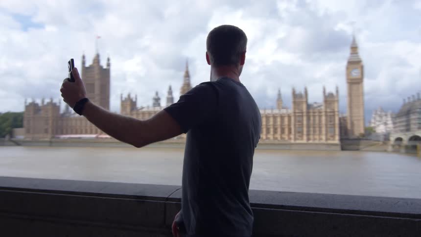 A man taking selfies with his cellphone showing a large castle behind him