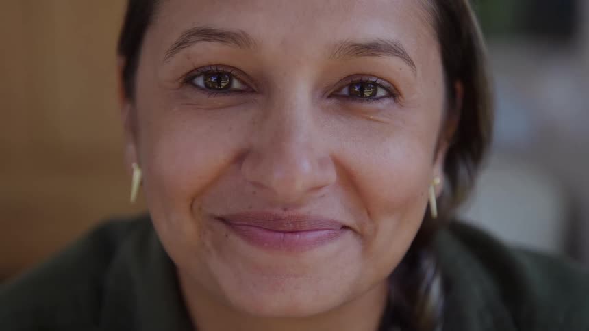 The face of a woman with brown eyes and light skin who maintains direct eye contact with the camera against a soft outoffocus background
