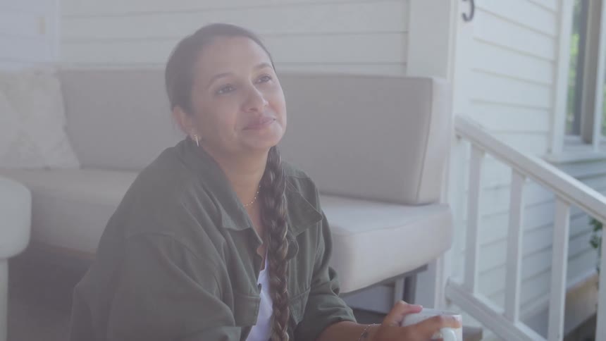 Woman smiling while holding a mug on a bright porch