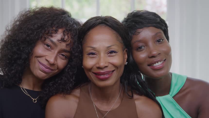 Three women smile together in a setting lit by natural light