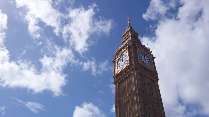 A majestic clock tower rises against a bright blue sky dotted with fluffy white clouds