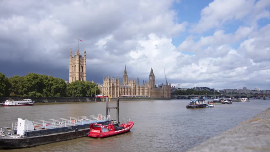 Boats travel on the river thames beside the palace of westminster under a cloudy sky