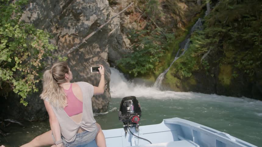 A woman sitting on the edge of a boat films the rushing water