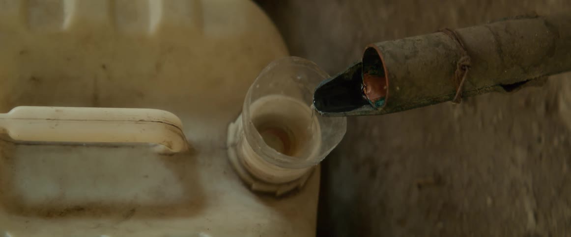 Pipe sticking out of an earthen wall releases water into the mouth of a large water storage container