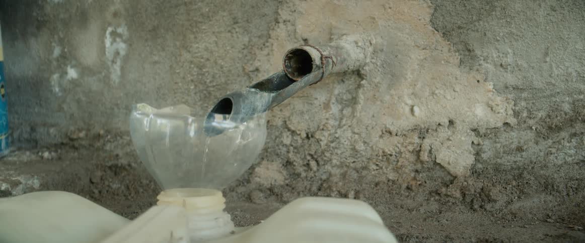Water trickles from a pipe sticking out of a wall into a clear bowl