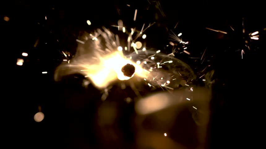 Sparks fly from a small flame burning in a dark area