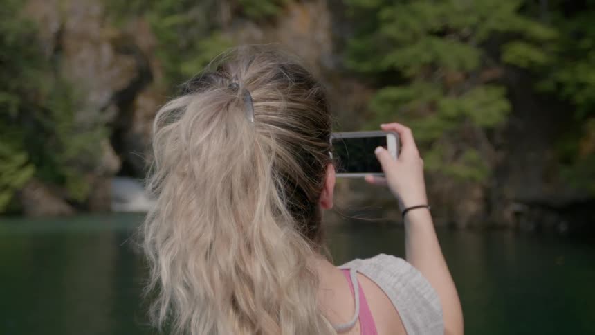 Woman taking a picture of a secluded lake with her smartphone