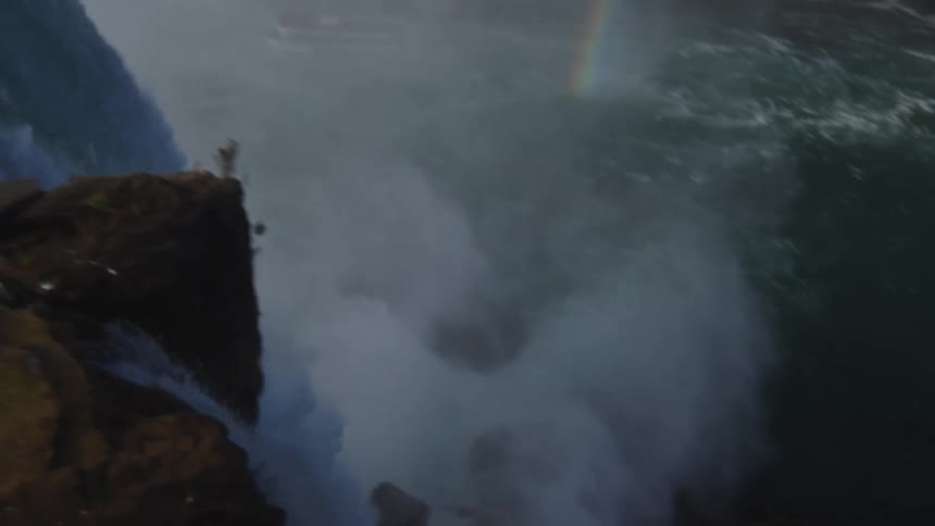 Water flowing over a cliff forms a large waterfall before falling into a large churning pool