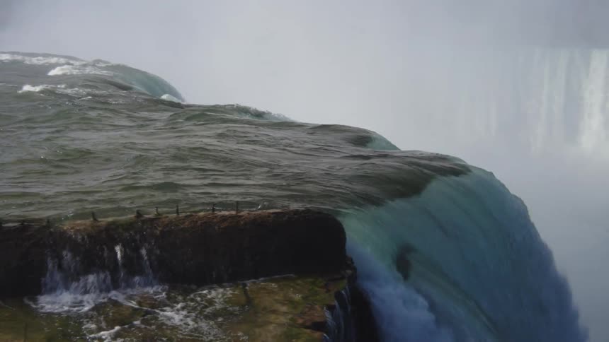 A waterfall cascading over some rocks and the water droplets are forming a rainbow in front