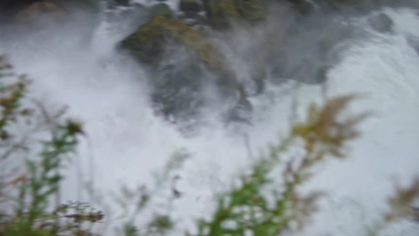 A waterfall cascades violently from a rocky mountain in the wild at midday