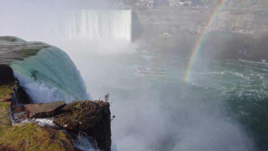 At the base of several waterfalls is a rainbow emerging from the river