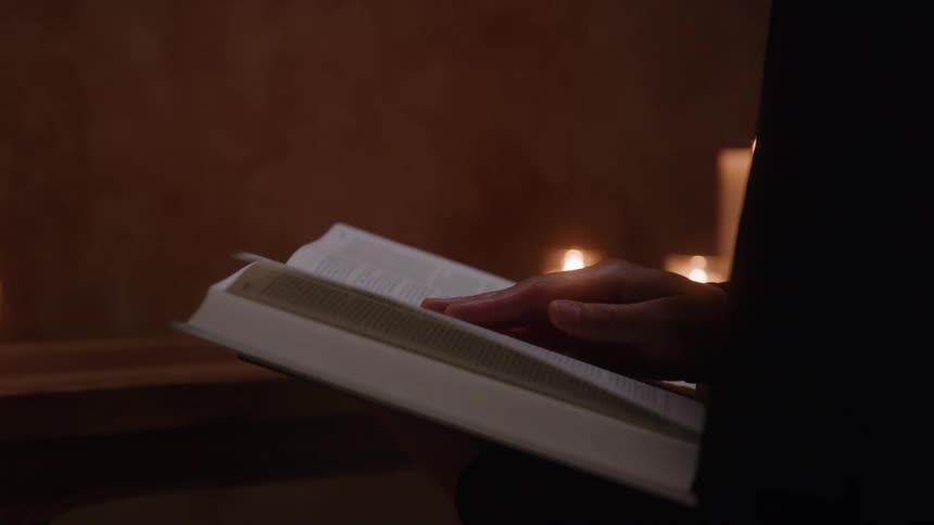 Woman standing in a room lit by candlelight flips through a book