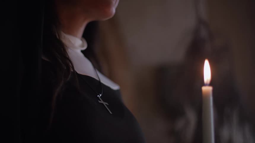 A person wearing a necklace with a cross carrying a lit candle indoors