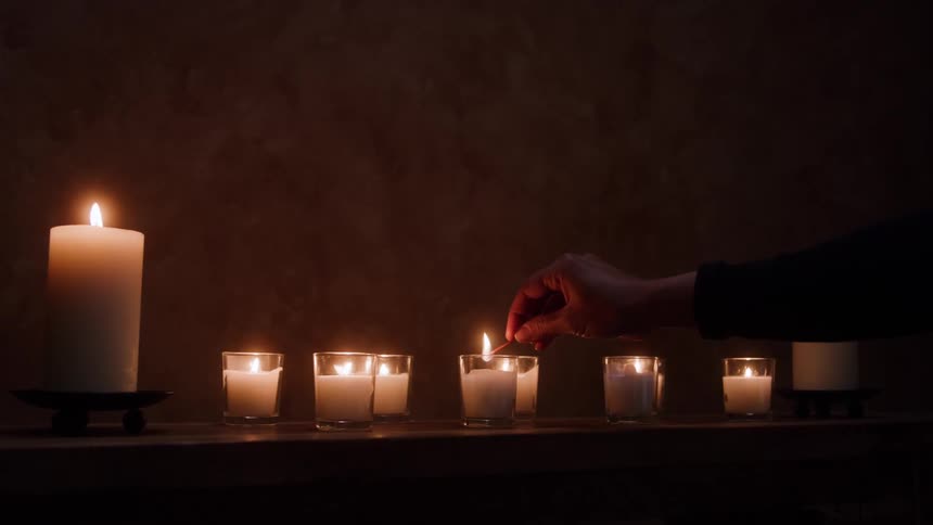 A closeup of hands lighting candles in a dimly lit room
