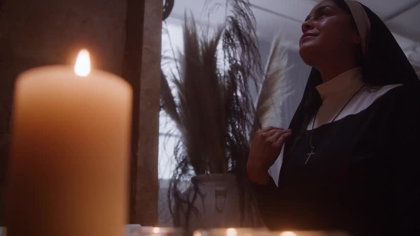 Nun praying in front of lit candles in a quiet setting