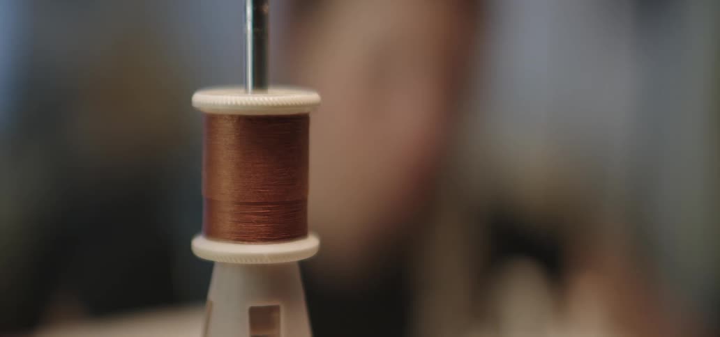 A brown thread spool on a white holder in sharp focus against a softly blurred background