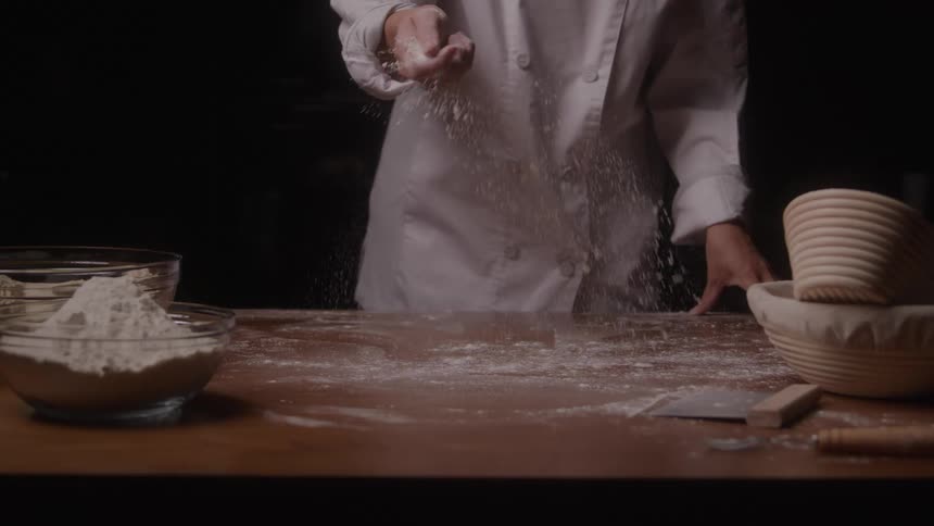 The chef sprinkles flour on the table