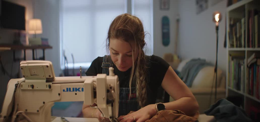 A woman focuses on sewing fabric with a machine in a cozy home workspace